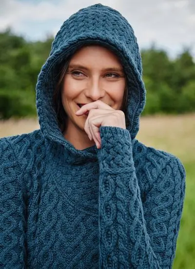 Close-up of brunette model in grassy area wearing a blue Aran biker hoodie with hood up.